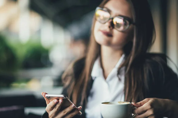 模糊的年轻女孩喝晨咖啡和看在咖啡厅的智能手机 — 图库照片