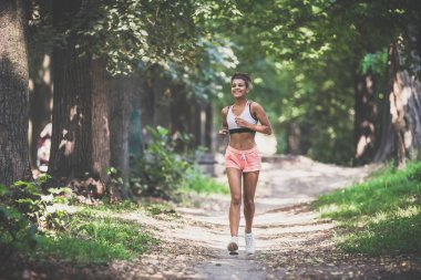 Genç fitness kadını orman yolunda koşuyor.