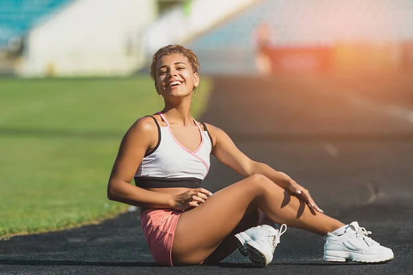 Mujer joven en ropa deportiva se sienta en la pista del estadio después del entrenamiento. estilo de vida saludable. sol de fondo — Foto de Stock