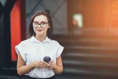 Gözlük takan ve açık havada kahve içme genç çekici işkadını Close-up. Güneş arka plan