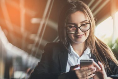 Mutlu genç kadın cep telefonuyla bir kahve ile bir masada oturuyor. Güneş arka plan
