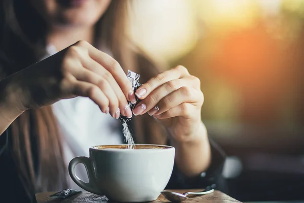 Ženská ruka nalévá cukr do kávy. Slunečnímu záření pozadí — Stock fotografie