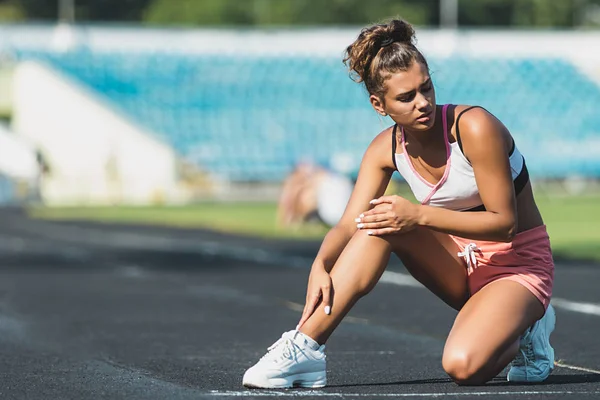 Esporte mulher se machucar nas pernas no estádio — Fotografia de Stock