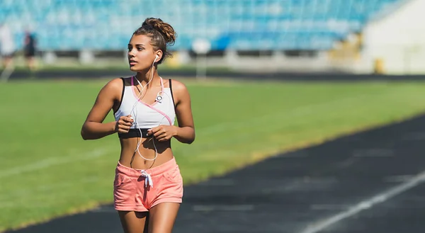 Retrato de atraente jovem e feliz fitness menina jogging enquanto ouve música no estádio — Fotografia de Stock