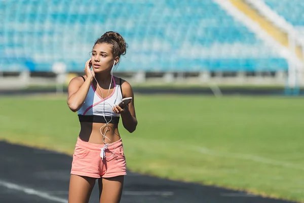 Corredor descansando en pista de atletismo al aire libre cansado tomando un descanso conseguir determinación y motivación listo para el desafío. Atleta mujer escuchando música con auriculares — Foto de Stock