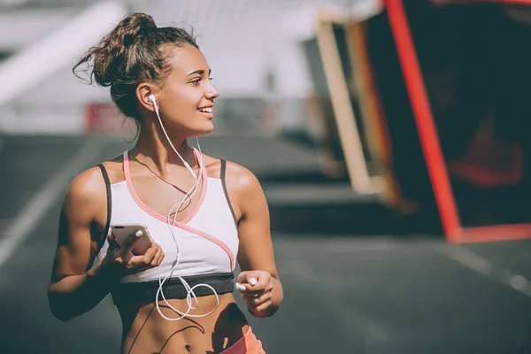 Jovem mulher apta a ouvir música e treinar correndo em pista de estádio urbano. Fechar — Fotografia de Stock