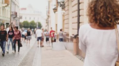 Onun akıllı alışveriş torbaları kollarında ile güneşli sokakta bahseden bir güzel genç kadın. Arkadan görünüm