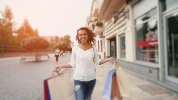 Piękna kobieta uśmiechający się ulicą. zwolnionym tempie. Piękna kobieta idzie przez miasto z torby na zakupy — Wideo stockowe