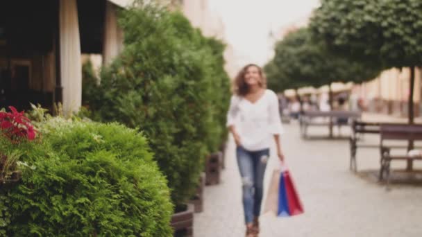 Happy fashion-monger woman with shopping bags walking down the street — Stock Video