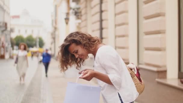 Mulher de compras de moda abre um pacote com compras, enquanto caminha pela rua da cidade. compras, tempo de compras — Vídeo de Stock