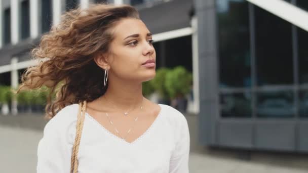 Retrato lateral de una joven de pie en la ciudad y el viento tocan su cabello — Vídeos de Stock