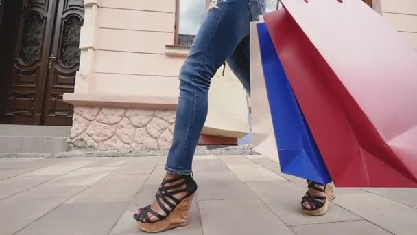 Vista lateral de uma mulher compradora de moda pernas andando com sacos de compras coloridos na rua. Movimento lento — Vídeo de Stock