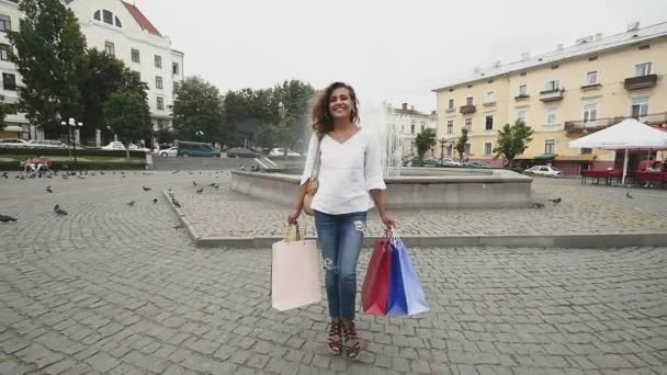 Mujer joven con bolsas de compras caminando por la calle de la ciudad. Movimiento lento — Vídeo de stock
