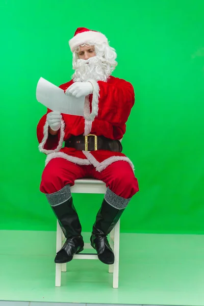 Портрет счастливого Санта-Клауса, читающего Рождественское письмо на зеленом фоне — стоковое фото