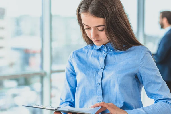 The secretary with a folder and documents is in the office. During this she is on the background of her colleagues. — Stok fotoğraf