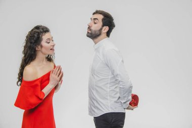 Young couple loving. A man made a present for his wife. During this time, the red field is presented in the form of a heart. Wife is pleasantly surprised. Dressed in a red dress and a white shirt.