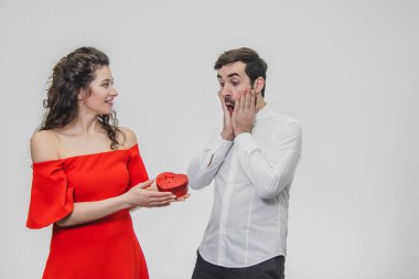 Young couple loving. A man made a present for his wife. During this time, the red field is presented in the form of a heart. Wife is pleasantly surprised. Dressed in a red dress and a white shirt.