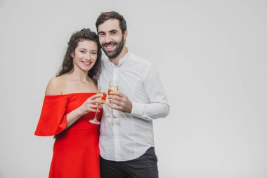 Seven genç çift şampanya içer. Beyaz bir arka plan üzerinde. Kırmızı elbise ve beyaz gömlek giymiş.