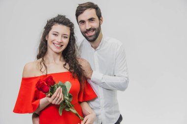 Zarif adam güzel bir kadın kırmızı bir elbise ve kırmızı gül buketi verir. Seven çift beyaz bir arka plan üzerinde.