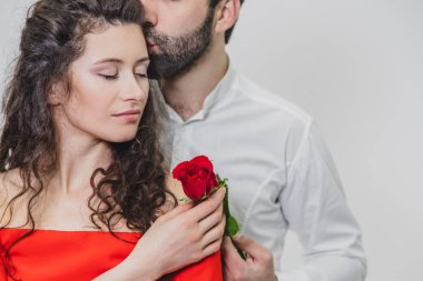 Genç ve yakışıklı bir adam güzel karısını nazikçe örter. Bu süre zarfında, bir kırmızı gül. Kız kırmızı bir elbise giymiş, beyaz gömlekli bir adam. Beyaz arka planda.