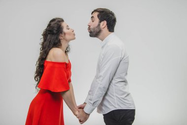 Genç ihale ve aşk kaç içinde. Birbirlerine ellerini öpmek isteyen düz bakmaya devam et. Kırmızı elbise ve beyaz gömlek giymiş. Beyaz bir arka plan üzerinde.