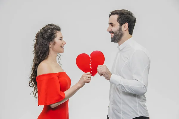 Retrato de um jovem casal amoroso. Um homem está vestido com uma camisa branca, sua esposa com um vestido vermelho. Realização de duas partes do papel do coração . — Fotografia de Stock