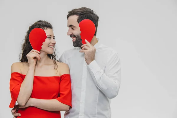 Retrato de um jovem casal amoroso. Um homem está vestido com uma camisa branca, sua esposa com um vestido vermelho. Realização de duas partes do papel do coração . — Fotografia de Stock