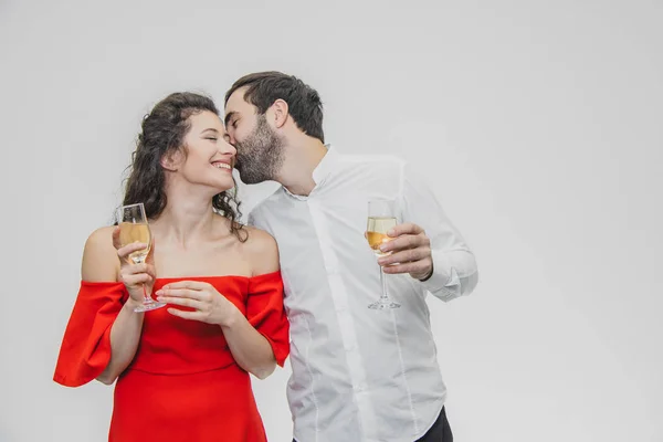 Kärleksfull ungt par dricker champagne. På en vit bakgrund. Klädd i röd klänning och vita skjortan. — Stockfoto