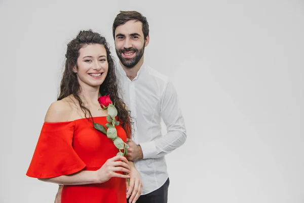 Un homme élégant donne à une belle femme une robe rouge et un bouquet de roses rouges. Couple aimant sur fond blanc . — Photo