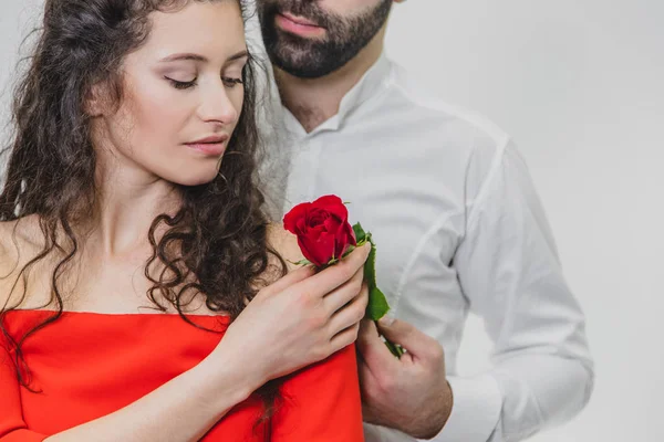 Un jeune et beau homme couvre doucement sa belle femme. Pendant ce temps, une rose rouge. La fille est vêtue d'une robe rouge, un gars en chemise blanche. Sur fond blanc . — Photo