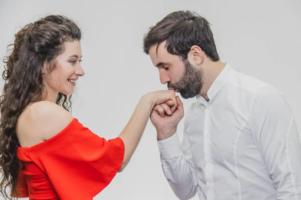 Jovem menino bonito beija sua linda menina lindamente. Durante esta menina vestida com um vestido vermelho, um cara em uma camisa branca . — Fotografia de Stock