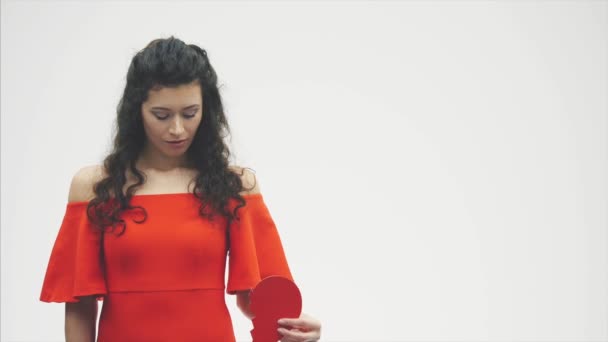 Retrato de una hermosa mujer sobre un fondo blanco. Día de San Valentín malo. El concepto, el modelo sostiene un corazón roto rojo en sus manos . — Vídeos de Stock