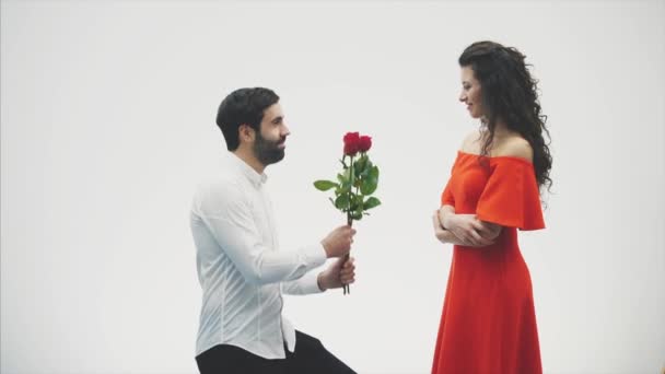 Piękna romantyczna para na białym tle. Atrakcyjna młoda kobieta na sobie czerwone róże w sukience i pięknego człowieka w białej koszuli daje różanych z miłością i czułością. Walentynki — Wideo stockowe
