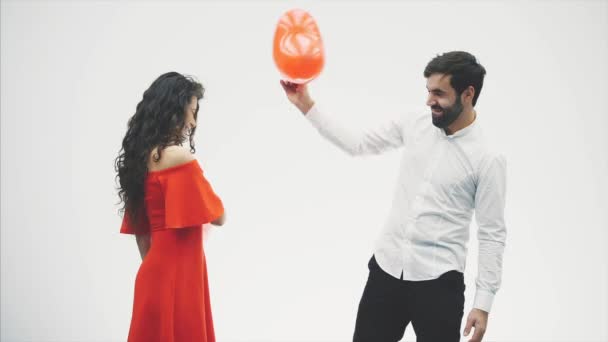 Hermosa pareja romántica aislada sobre fondo blanco. Una atractiva mujer joven y guapo golpean entre sí con globos en la forma del corazón en sus manos. Sonriendo. Feliz San Valentín — Vídeo de stock