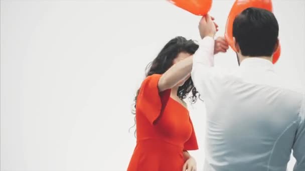 Beau couple romantique isolé sur fond blanc. Une jeune femme séduisante et beau frappent les uns les autres avec des ballons en forme de cœur dans leurs mains. Souriant. Joyeuse Saint Valentin — Video