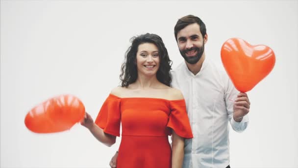 Beautiful romantic couple isolated on white background. An attractive young woman and handsome knock each other with balloons in the shape of the heart in their hands. Smiling. Happy Valentine — Stock Video