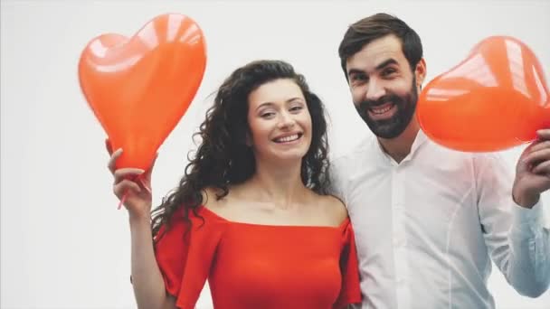 Beautiful romantic couple isolated on white background. An attractive young woman and handsome knock each other with balloons in the shape of the heart in their hands. Smiling. Happy Valentine — Stock Video