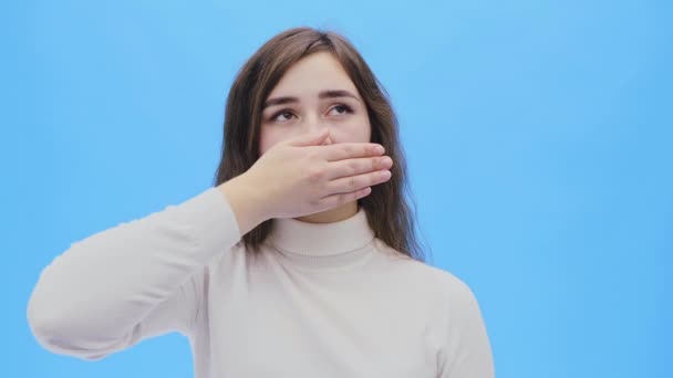 Beautiful young woman with clean, perfect skin.Looking straight the girl closes her mouth with her hand. — Stock Video