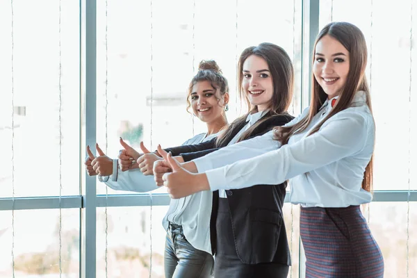 Tres chicas de negocios jóvenes en la oficina. Vestido en estilo de ropa clásica, mostrando los pulgares hacia arriba —  Fotos de Stock