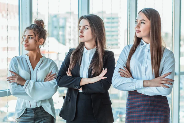 With pleasure, three business women cross their arms, looking at the camera.