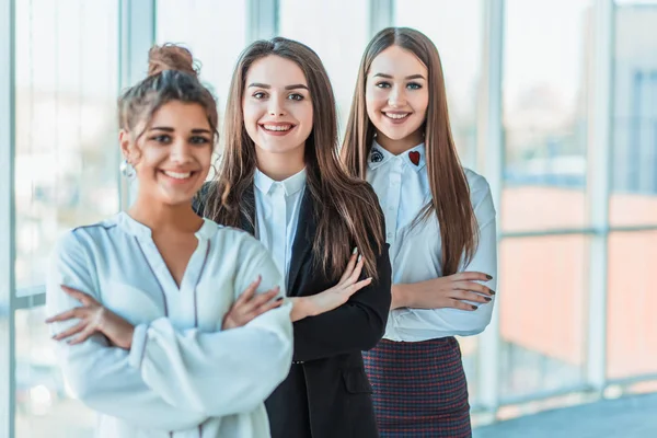 With pleasure, three business women cross their arms, looking at the camera. Dressed in white blouses copy space