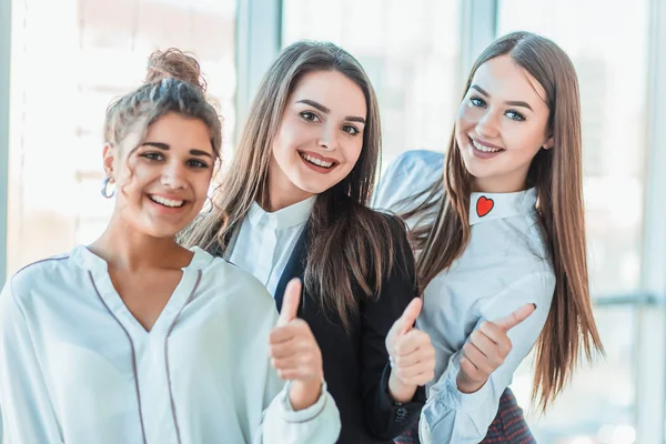 Three young business girls in the office. Dressed in classic clothing style, showing thumbs up with a gesture with copy space — Stock Photo, Image