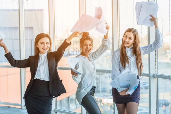 Three young beautiful brunette business ladies in the office. All happy dancing dancing up the documents up with