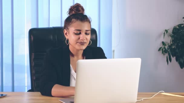 A menina está vestida com roupas elegantes, sentada no escritório e imprimindo informações em um laptop . — Vídeo de Stock