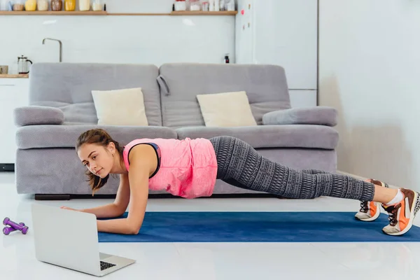 Young girl looking at laptop and doing exercises at home.