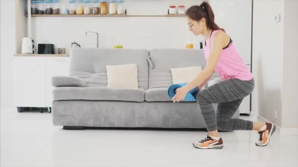 Close up van een jonge mooie vrouw gekleed in blauwe joggen of een fitness mat na het werken thuis in de woonkamer. — Stockvideo