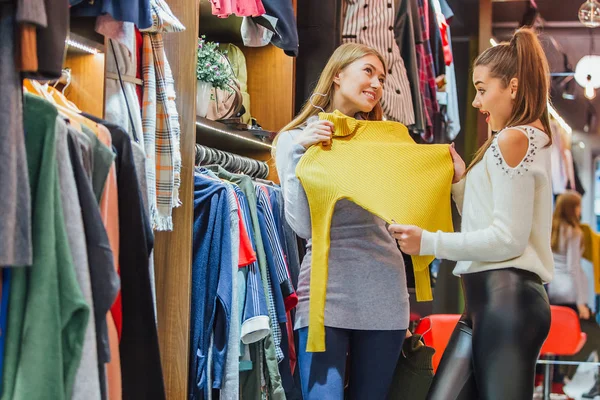 Dos amigos eligen suéteres durante las compras. Siéntete bien, sonriendo y riendo . — Foto de Stock