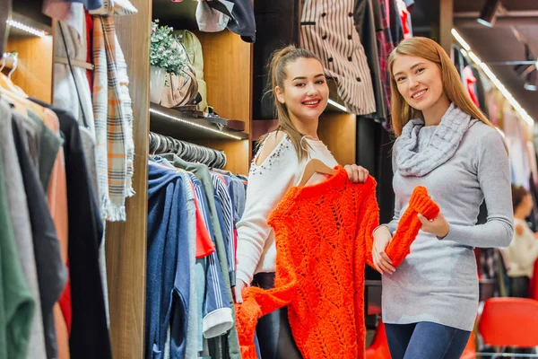 Two friends choose sweaters during shopping. Finding an orange girl sweater happy. Feel good, smiling and laughing. — Stock Photo, Image