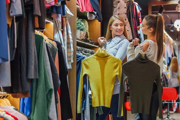 Two friends choose sweaters during shopping. Feel good, smiling and laughing. — Stock Photo, Image