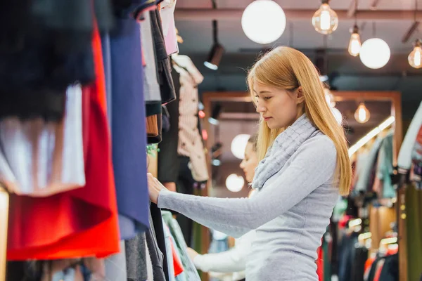 Mujer elige la ropa al comprar en una tienda de ropa — Foto de Stock